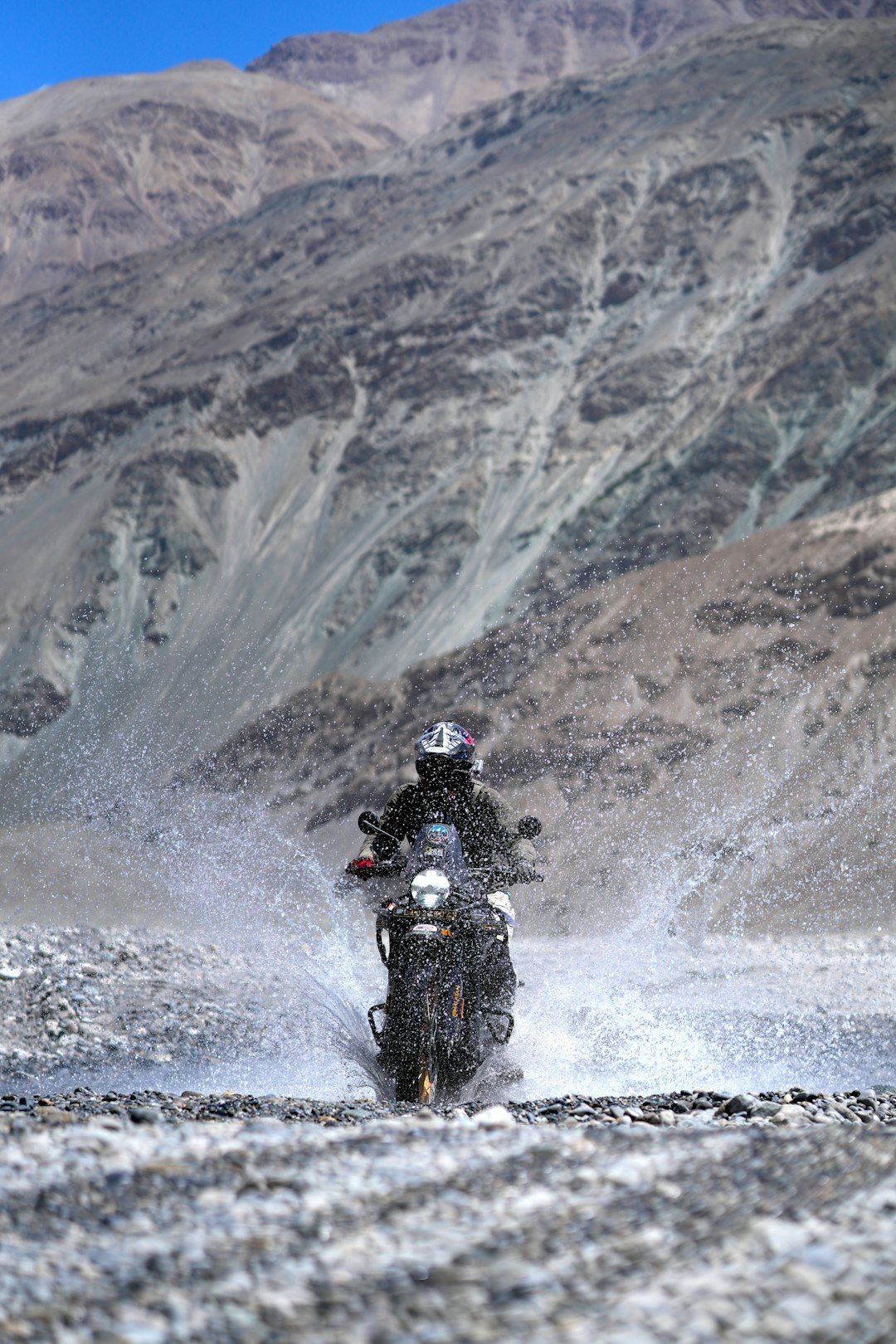 Motorcyclist riding through water in rocky terrain