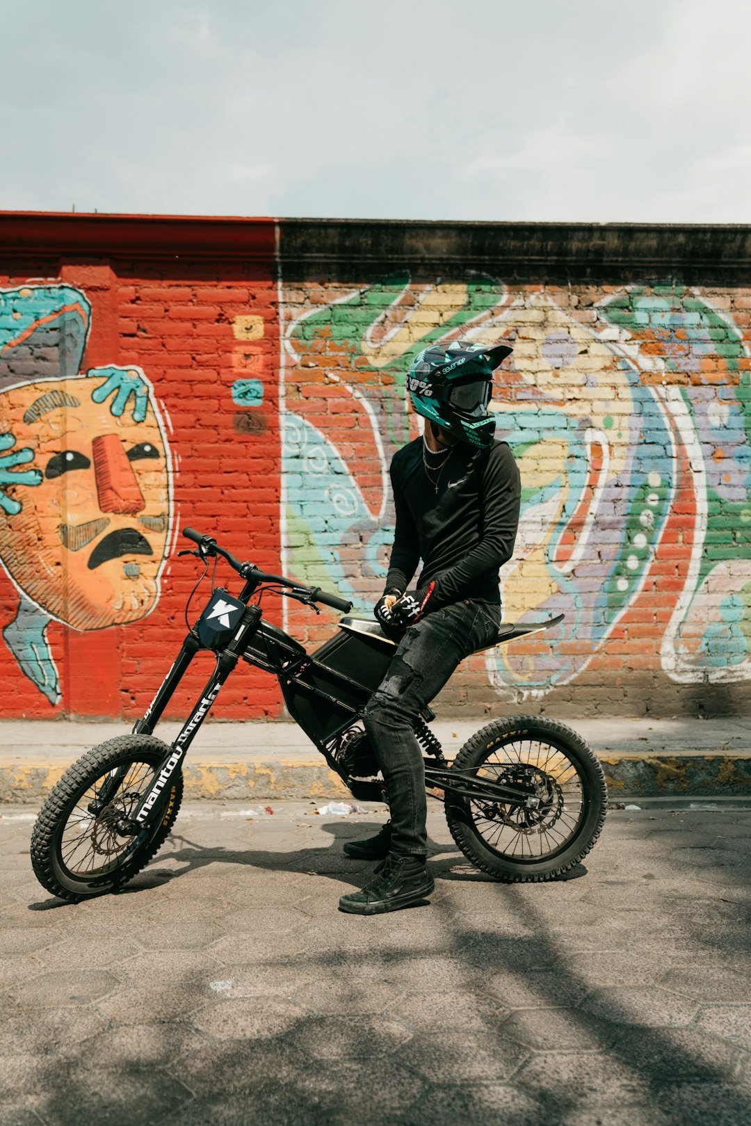 a man sitting on a dirt bike in front of a brick wall