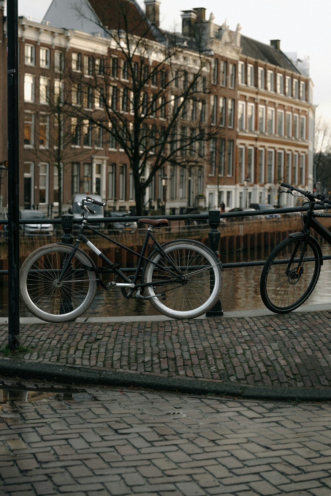 Bicycles are parked on a bridge by canal houses.