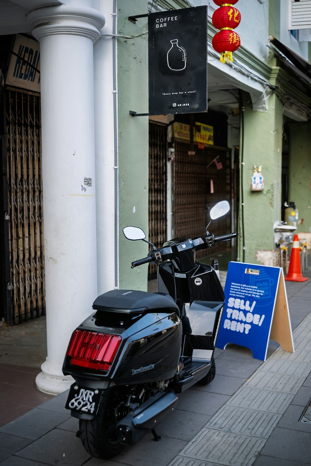 Black scooter parked outside a coffee bar.