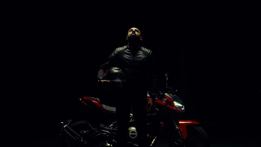 Man holding helmet beside motorcycle in darkness