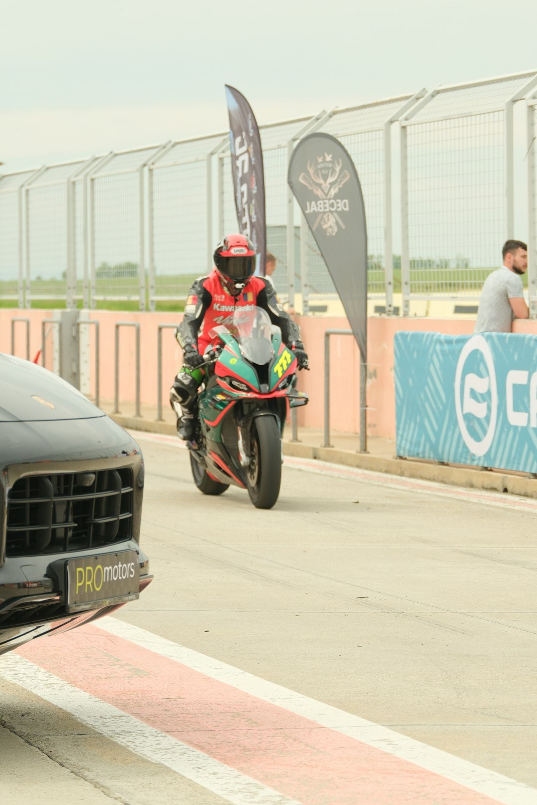 Motorcyclist in red gear rides a green and black motorcycle.