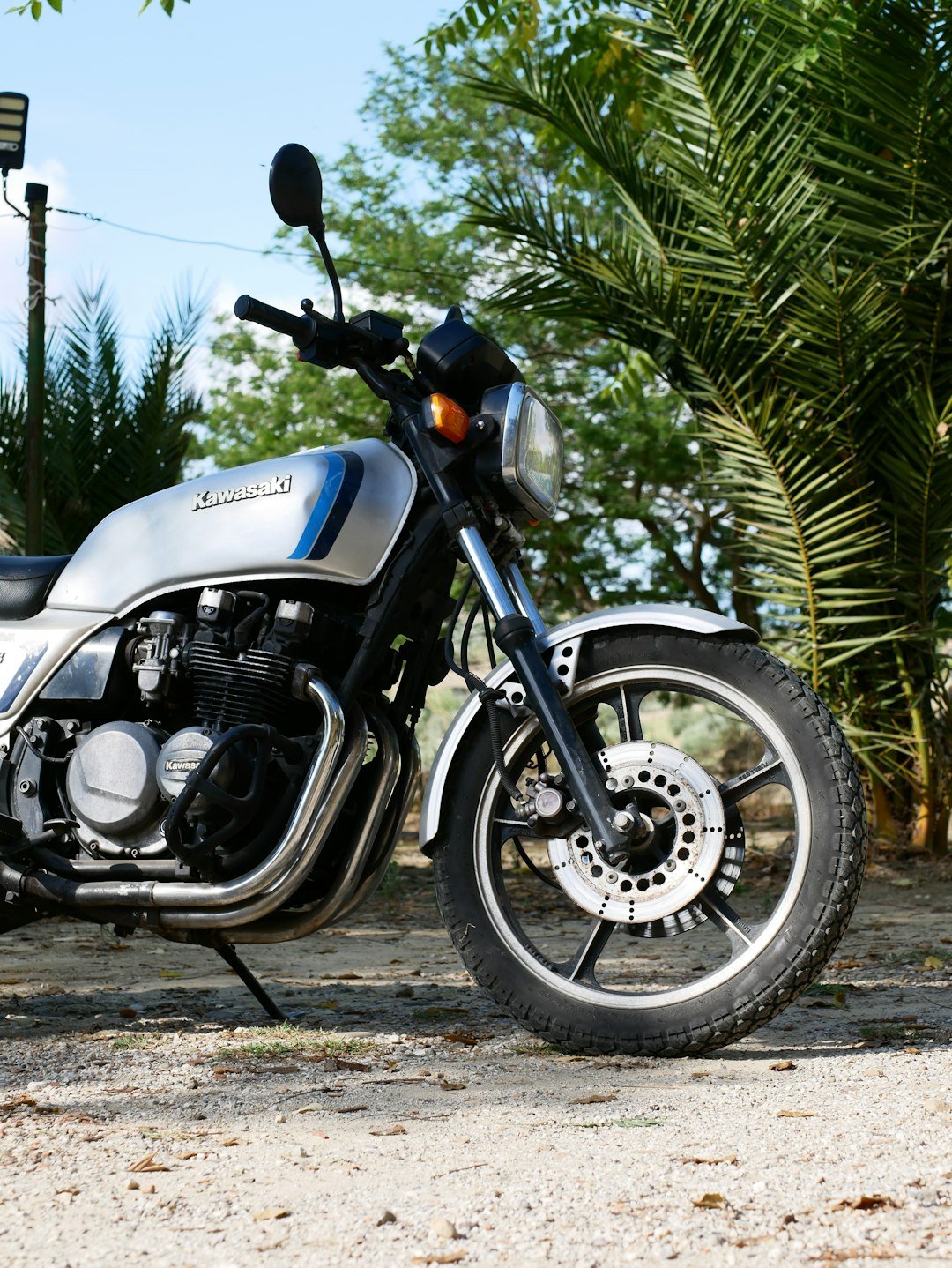 A silver motorcycle parked outdoors with palm trees.