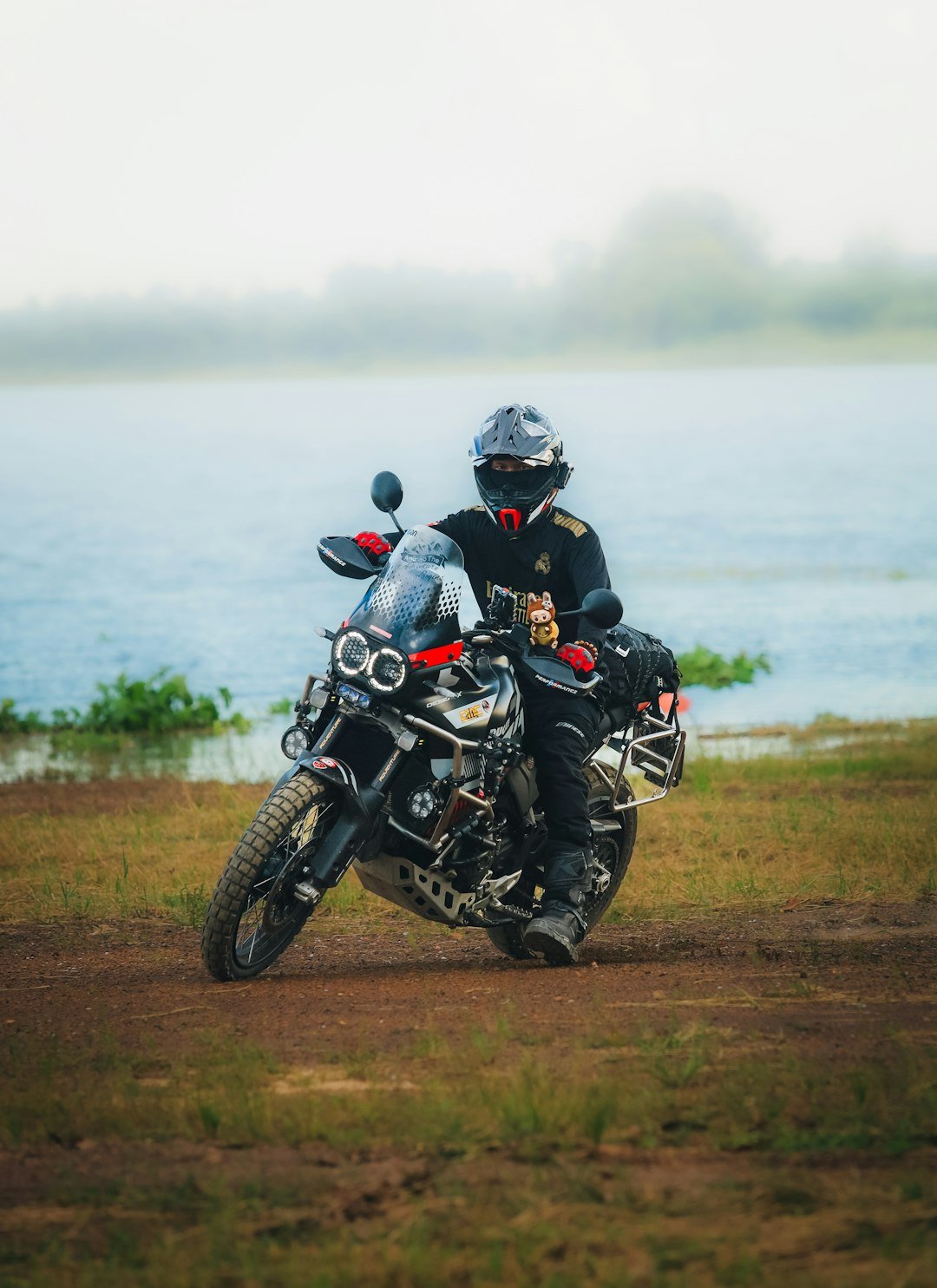 Motorcyclist on dirt road near water with fog.
