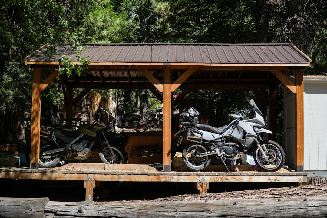 Two adventure motorcycles parked under a wooden shelter.