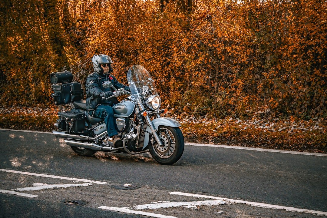 Man riding a motorcycle on a road with autumn leaves