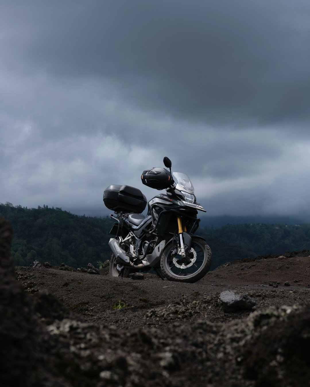 Motorcycle parked on rough terrain under cloudy sky.