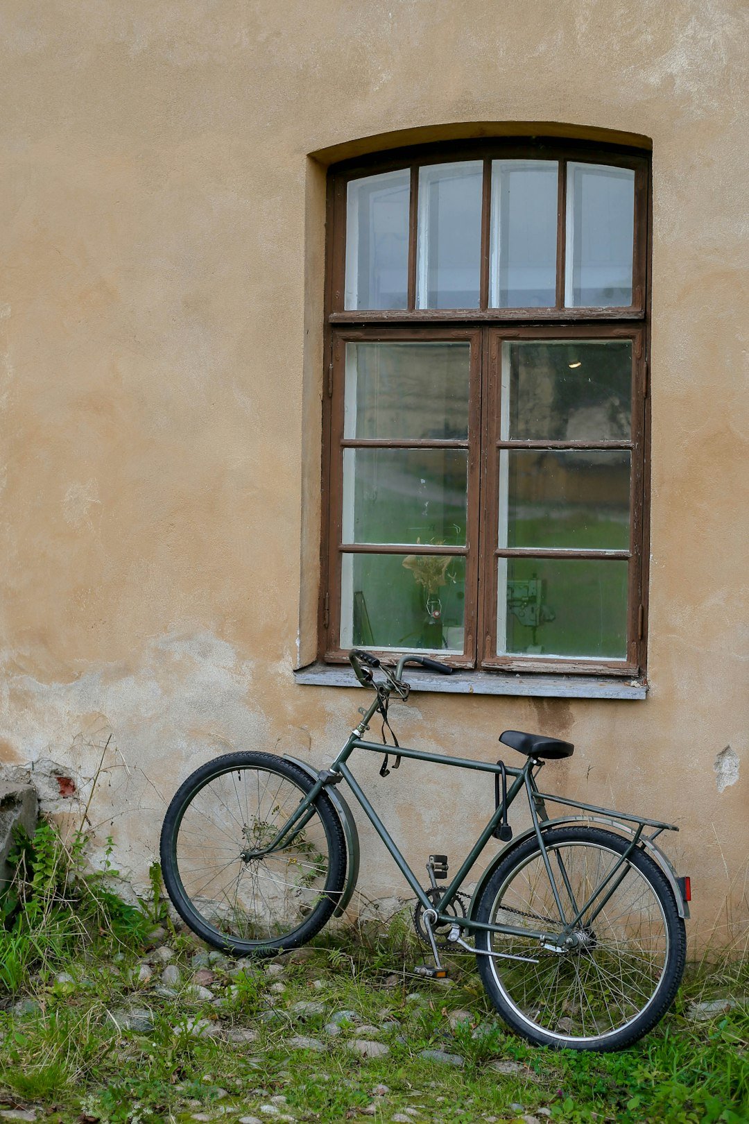 A bicycle leans against a weathered wall by a window.