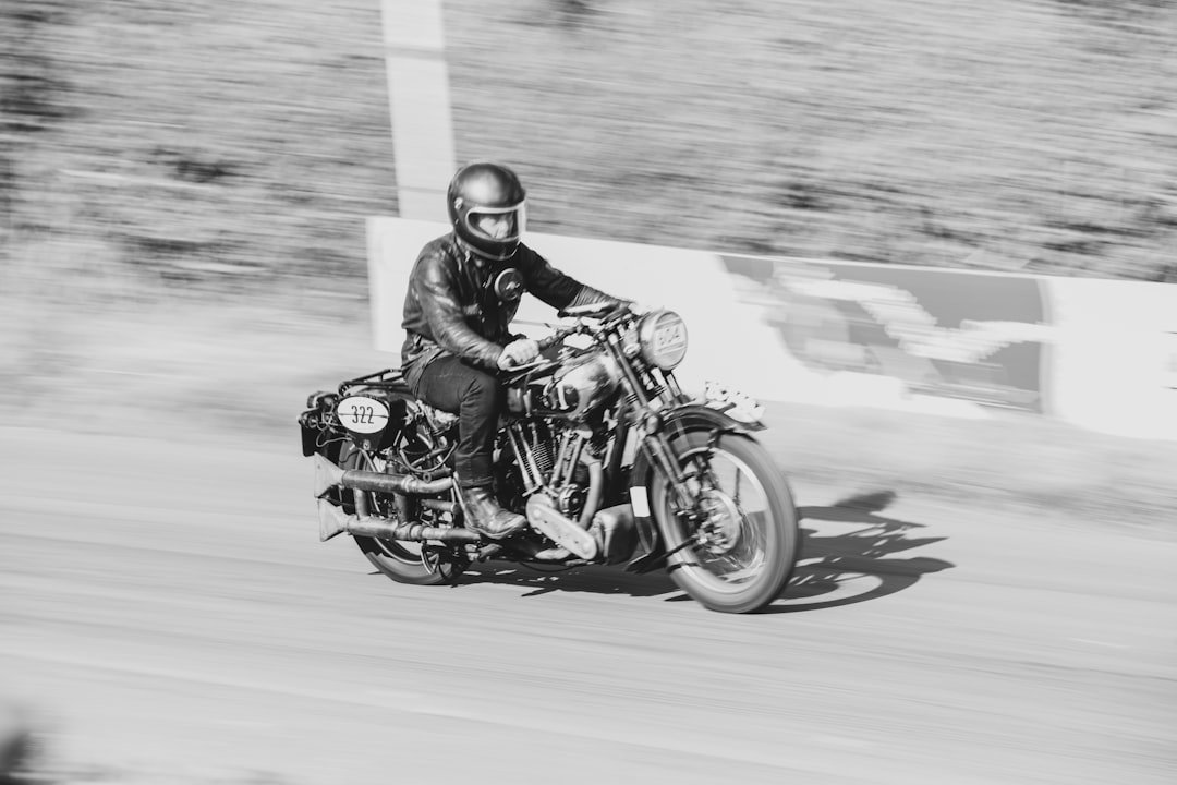 Man in helmet riding vintage motorcycle on dirt track.