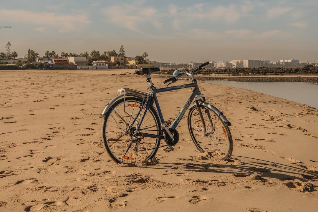 Bicycle parked on a sandy beach with buildings distant.