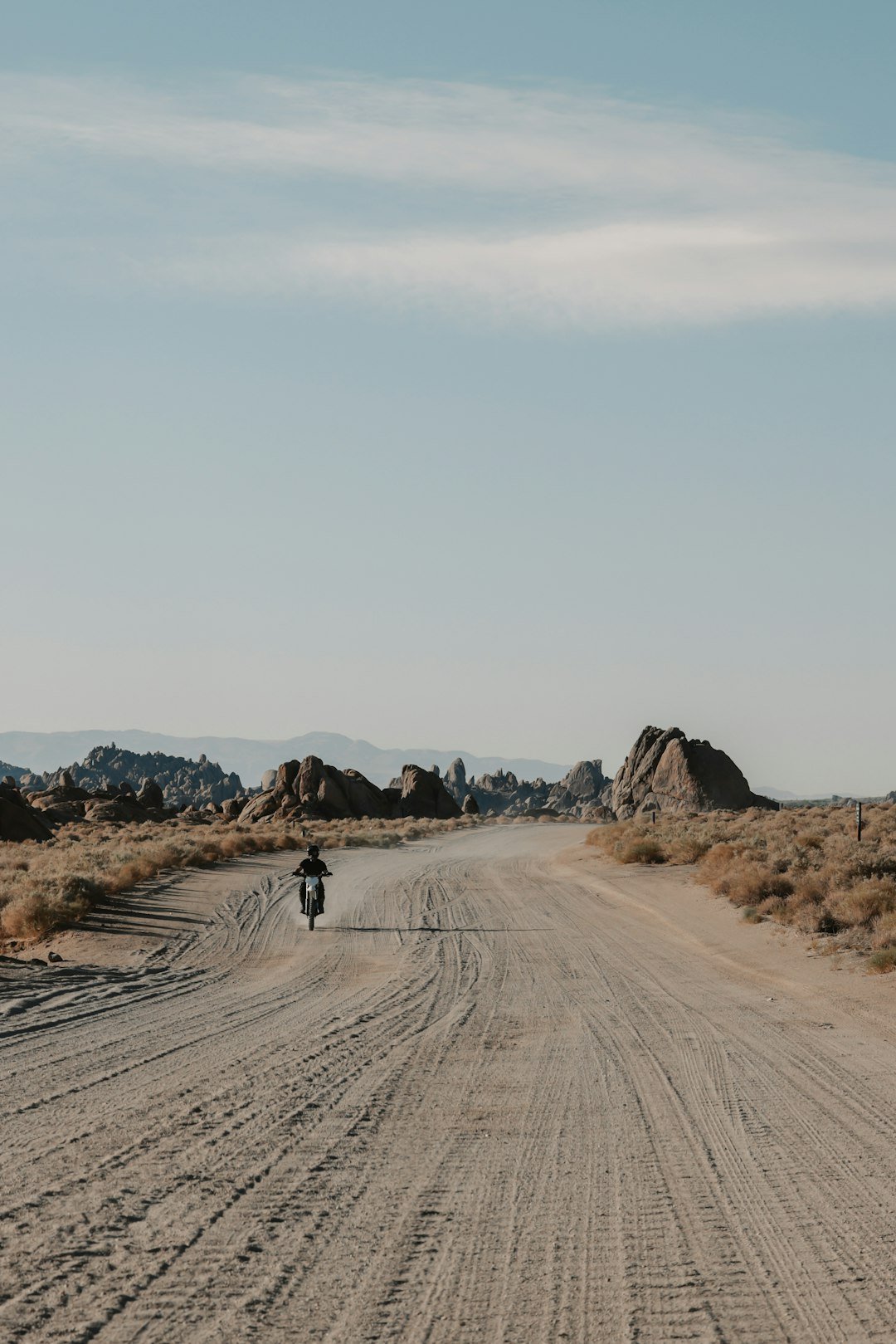 Motorcyclist rides on a dusty desert road.