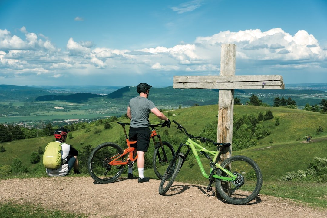 man in gray shirt and black pants standing beside black and red mountain bike during daytime