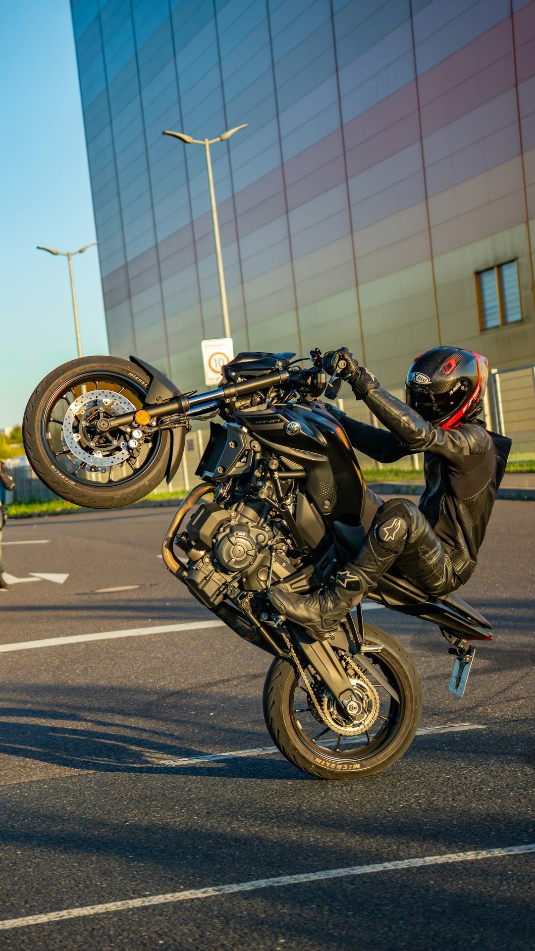 Motorcyclist performs a wheelie in front of a modern building.