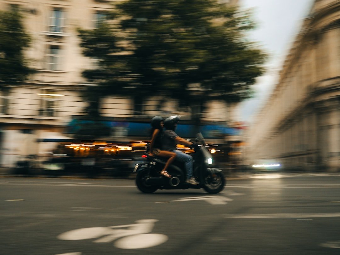 Two people riding a scooter through a city street.