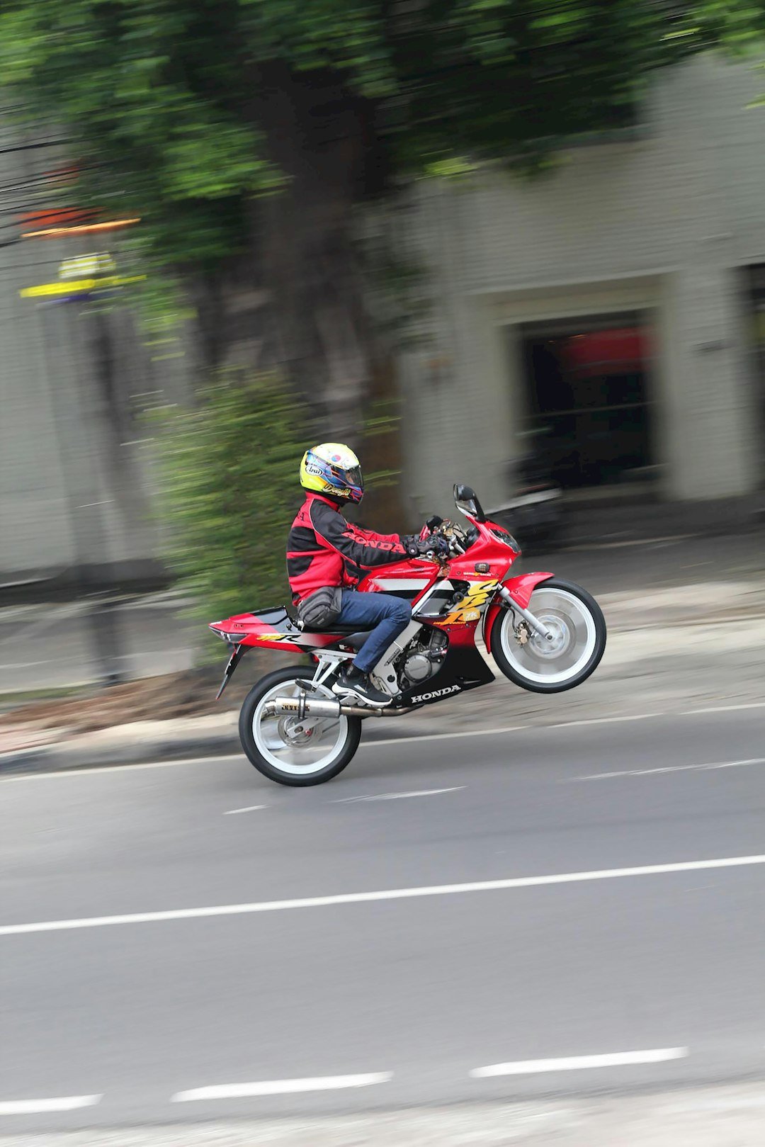 Motorcyclist performs a wheelie on a city street.