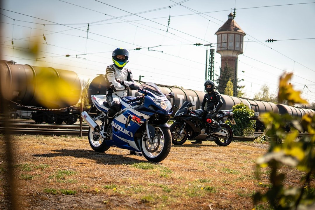 Two motorcyclists ride near a train track.