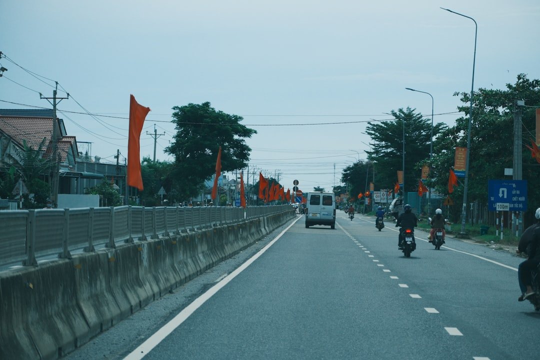 Orange flags line a road with vehicles and trees.
