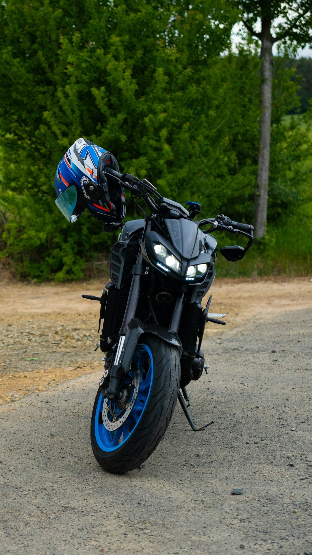 Black motorcycle with blue rims and helmet on handlebars.