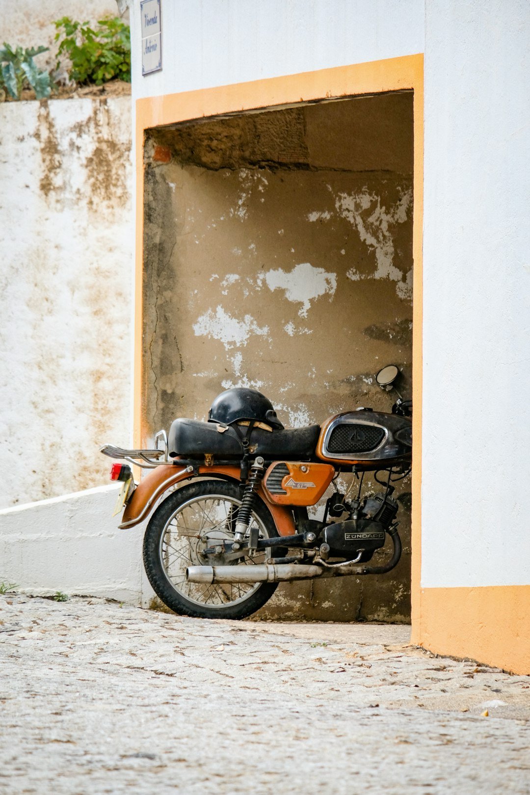 Orange motorcycle parked in a sheltered alcove.