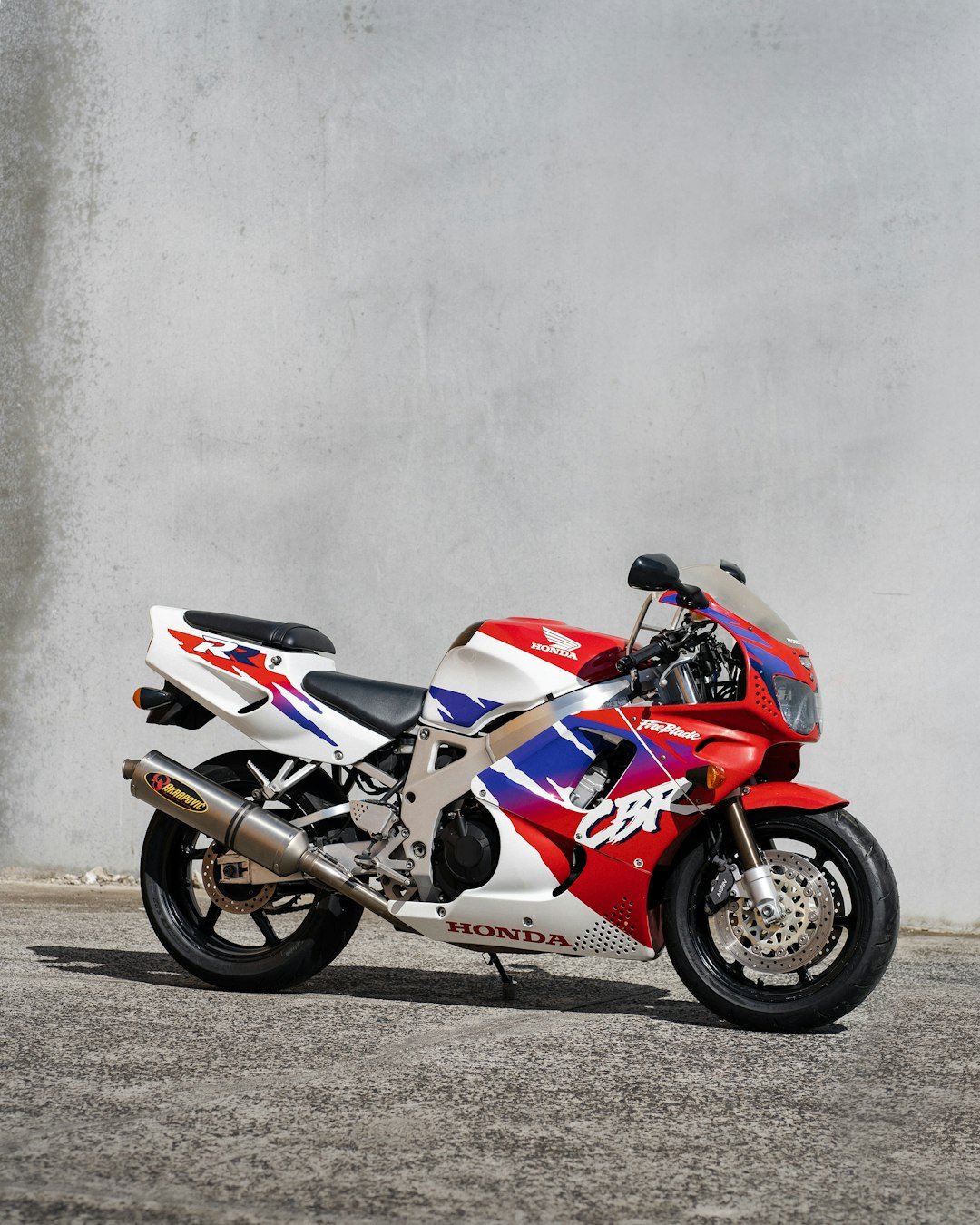 a red, white and blue motorcycle parked in front of a wall