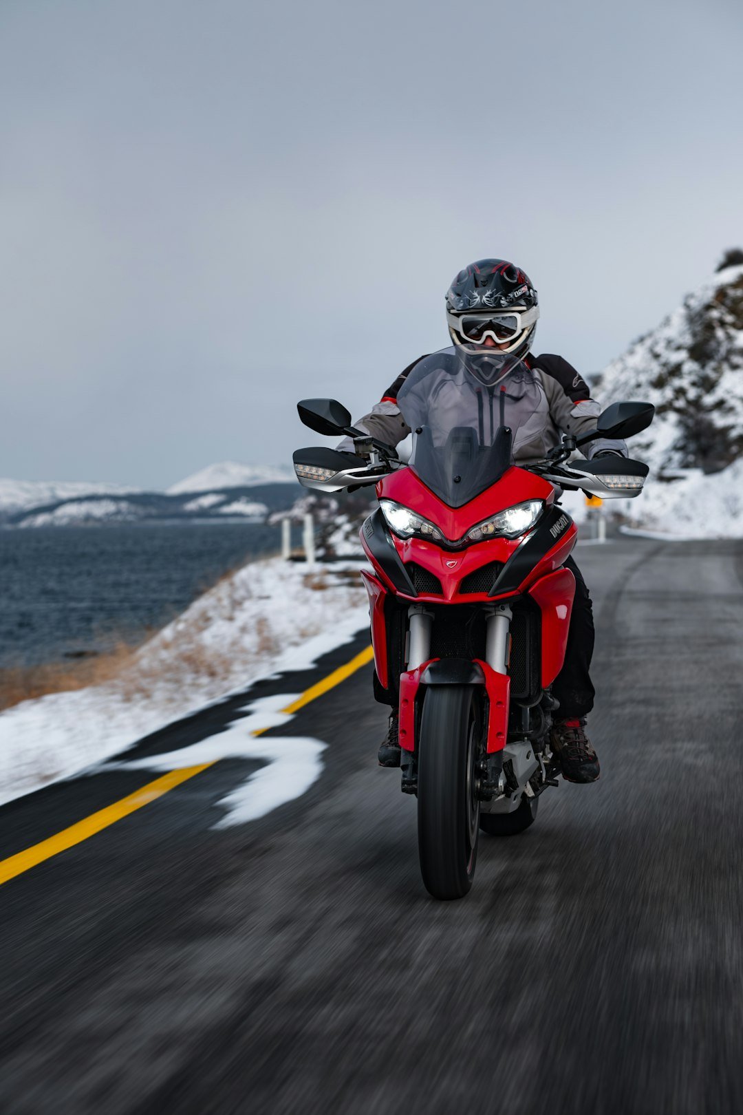 Rider on red motorcycle on snowy road near ocean